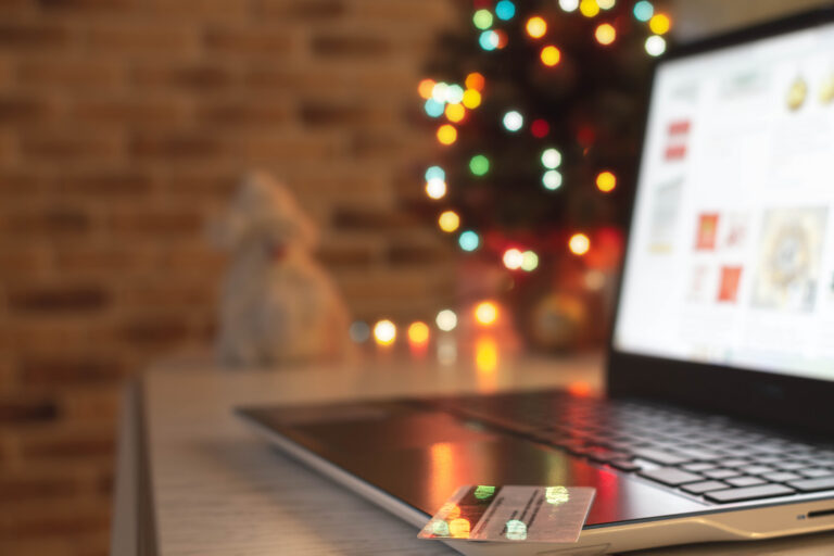 Christmas shopping online. Laptop and credit bank card on table at home on the background of a Christmas tree with blurred bokeh lights